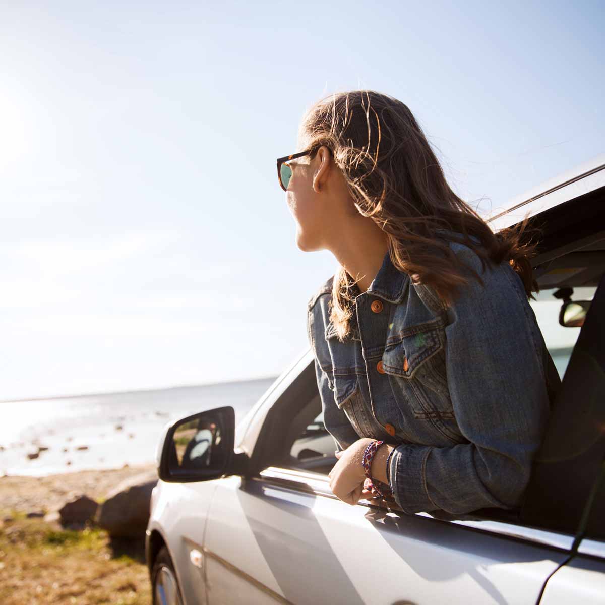 Woman hanging out the door of a Byron Bay rental car at the beach